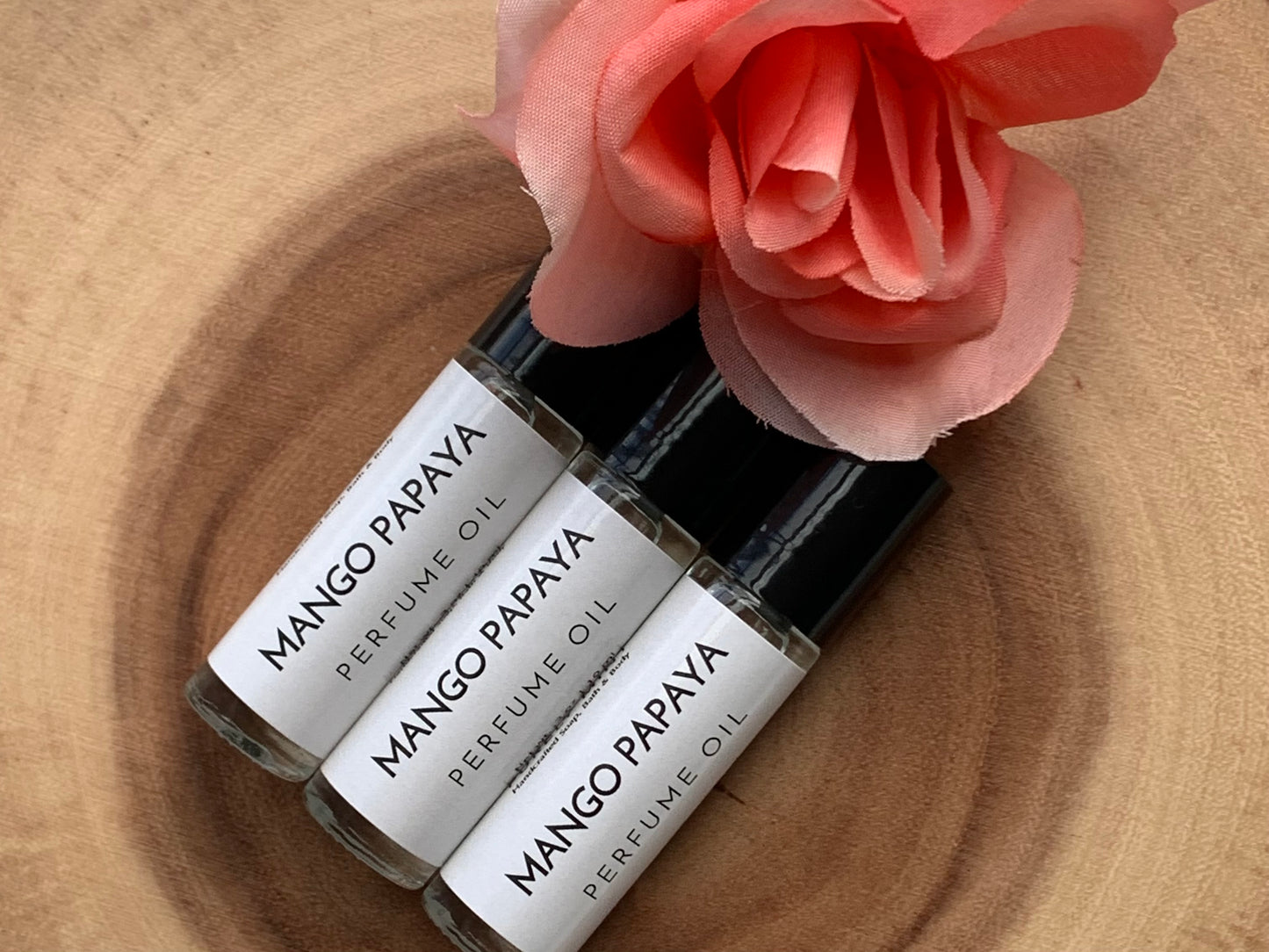 3 perfume roller on wood with pink flower.