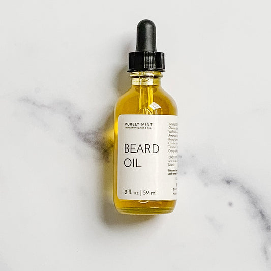 A 2 oz glass bottle of Gentlemen's Beard Oil with a dropper, placed on a marble surface